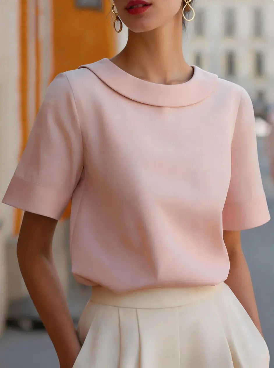 A women solid color short sleeve versatile top in soft blush pink featuring a rounded collar and smooth tailored fabric.