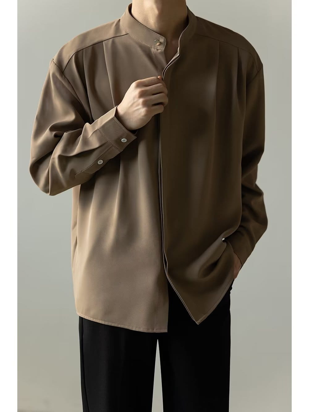 Chemise plissée pour homme à col montant en beige, présentant une coupe élégante à manches longues boutonnées, un col mandarin et des surpiqûres de contraste discrètes.
