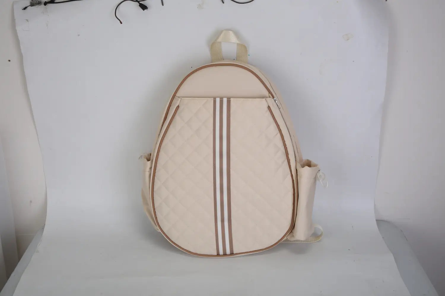 Sac bandoulière pour pickleball matelassé beige, imperméable, avec trois rayures verticales brunes et une poignée assortie, doté d’une poche humide.