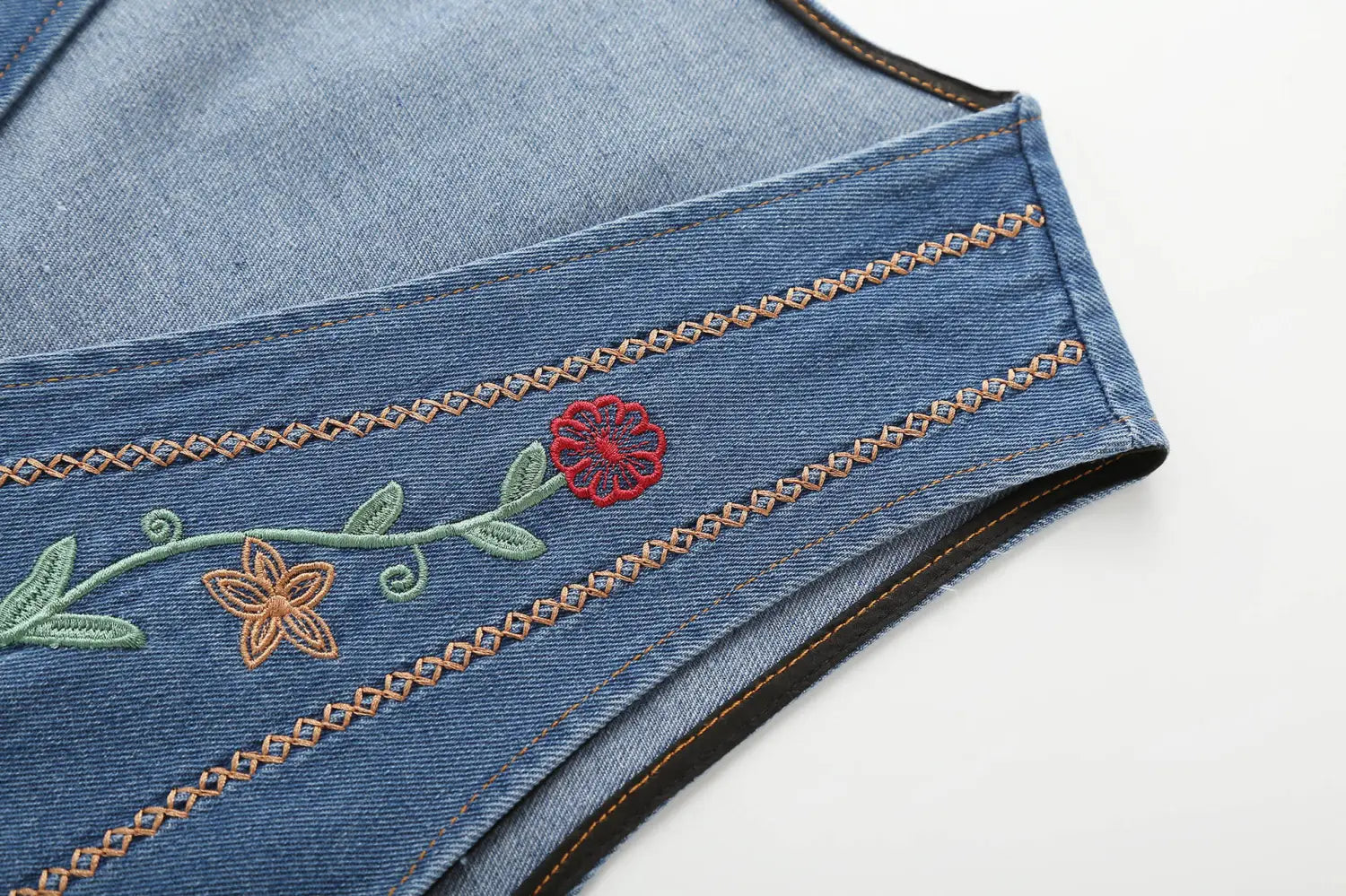 Bestickte florale Jeansweste mit einem Design aus rotem, grünem und beigem Faden auf blauem Jeansstoff.