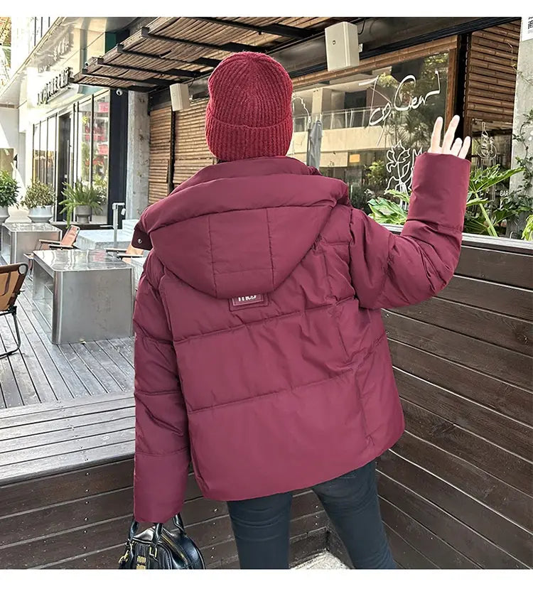 Veste courte matelassée bordeaux à capuche pour femme, avec des détails de surpiqûre discrets, conçue comme un manteau d’hiver chaud.