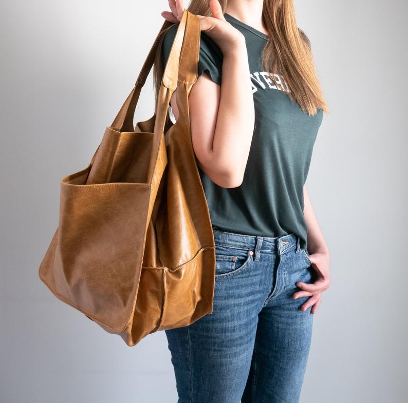 A tan leather tote bag with wide handles and a spacious slouchy design offering large capacity and soft shoulder comfort.