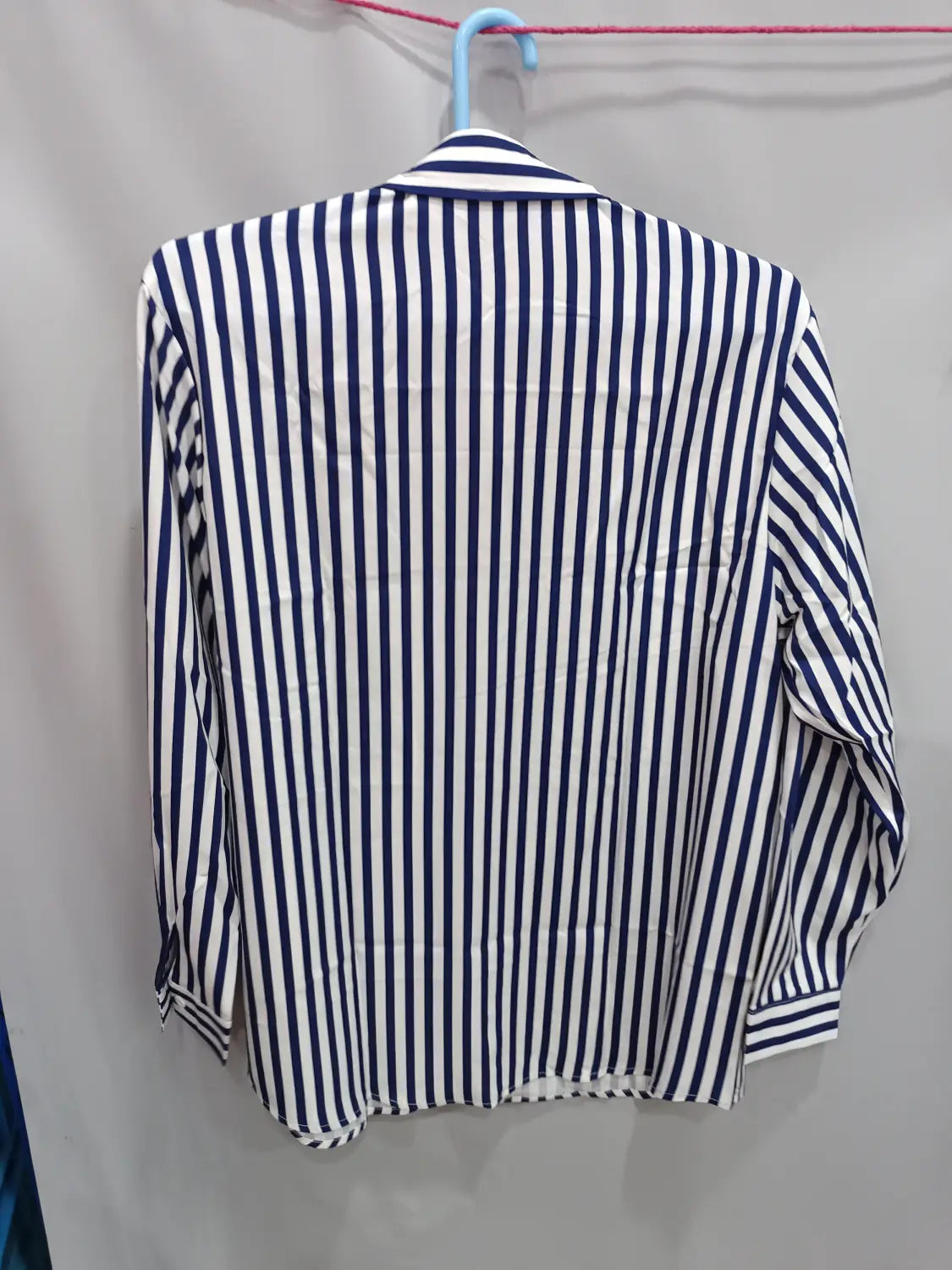 Chemise décontractée à manches longues rayée verticalement bleu marine et blanc pour hommes, présentée sur un cintre bleu.