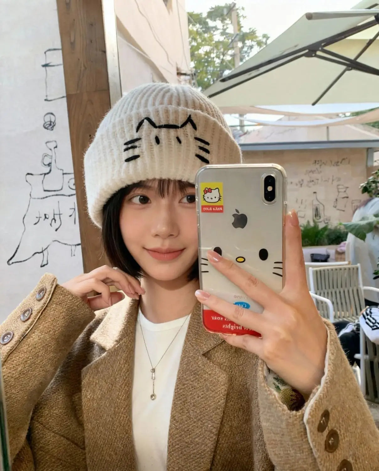Cream-colored knitted beanie hat featuring a black embroidered cat face design.