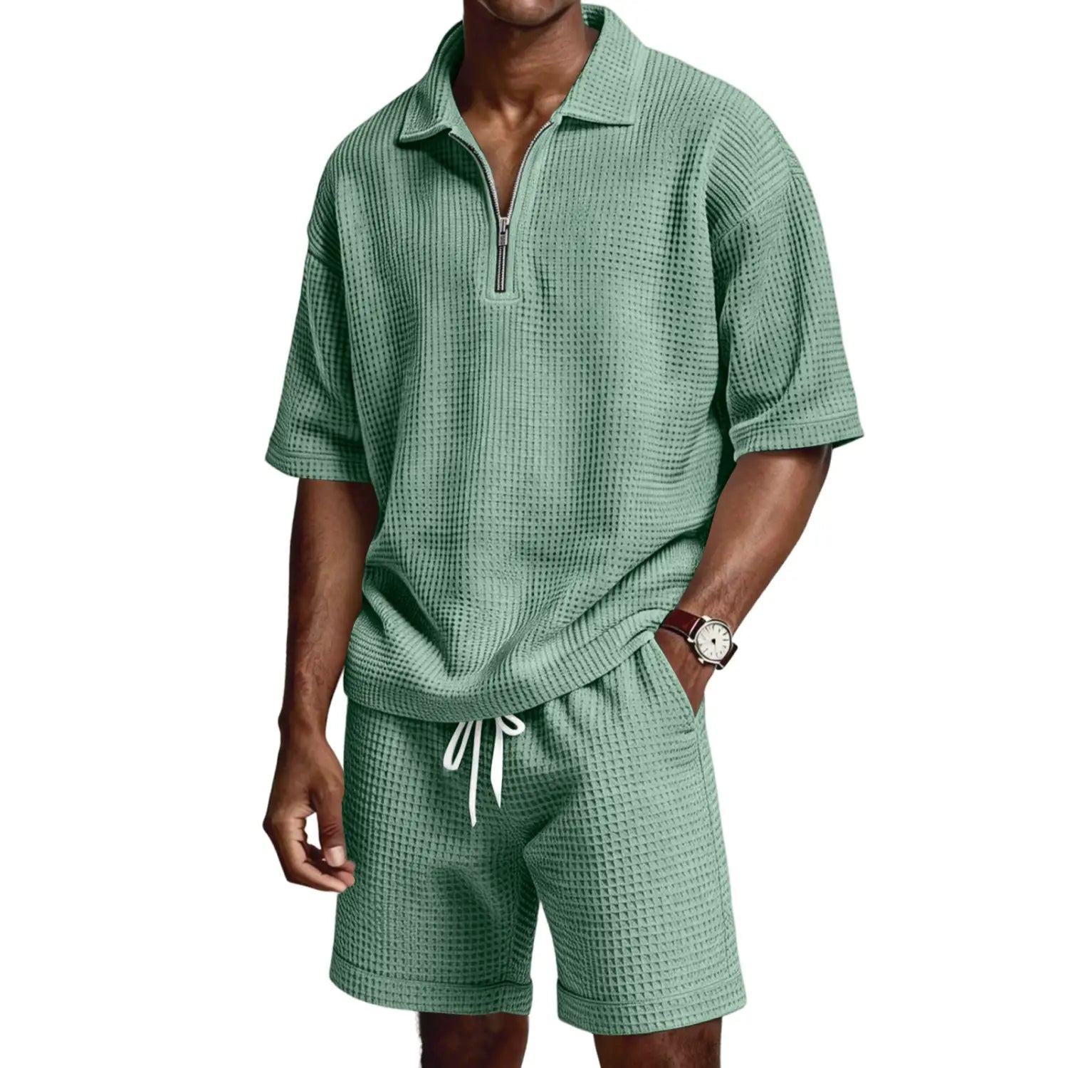 Un homme portant un ensemble short polo à demi-zip en maille nid d’abeilles vert menthe, composé de deux pièces, avec des manches courtes et un short doté de cordons blancs.