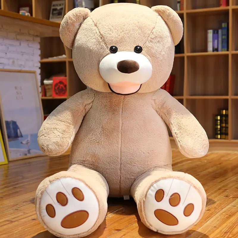 Ein großer Teddybär-Plüschartikel mit einer Größe von 1 Meter, mit weichem beigem Samt-Fell, schwarzen Knopfaugen, einem weißen Schnäuzchen und einer braunen Nase, der auf einem Holzboden sitzt.
