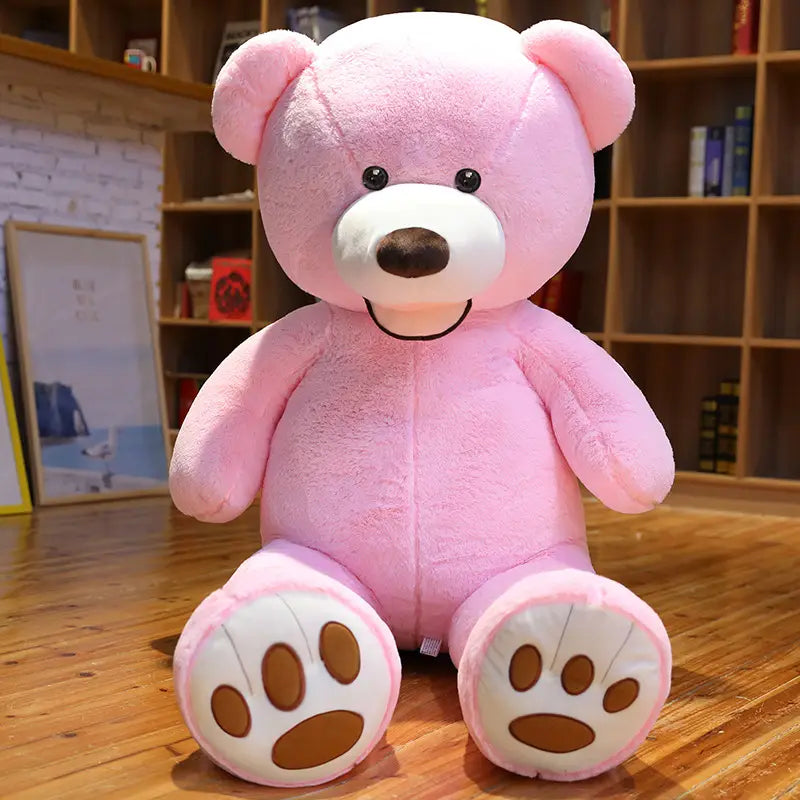 Ein großer Teddybär-Plüschartikel aus weichem rosafarbenem Samt mit weißen Pfoten und braunen Pfotenabdrücken, schwarzen Knopfaugen sowie einem angenähten Lächeln, mit einer Größe von einem Meter.