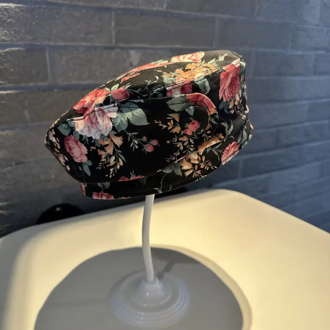 Black floral bucket hat with pink and peach blossoms displayed on a white stand in a printed Korean style fashion cap design.