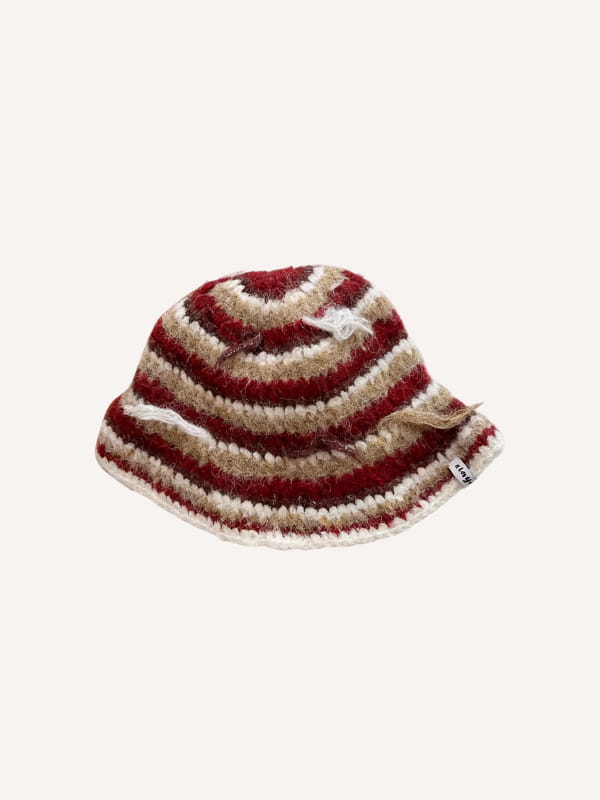 Un chapeau de pêcheur multicolore tricoté à la main, confortable, avec des rayures horizontales profondes rouge foncé et crème, fabriquées en fil, et présentant un bord légèrement effiloché.