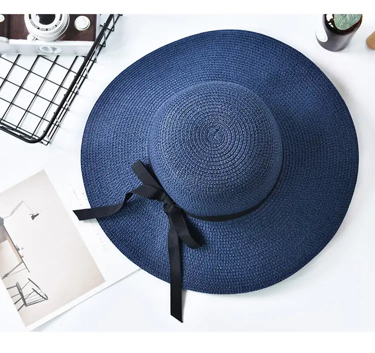 Wide brim straw sun hat in deep blue woven straw with a black ribbon bow at the base of the crown.