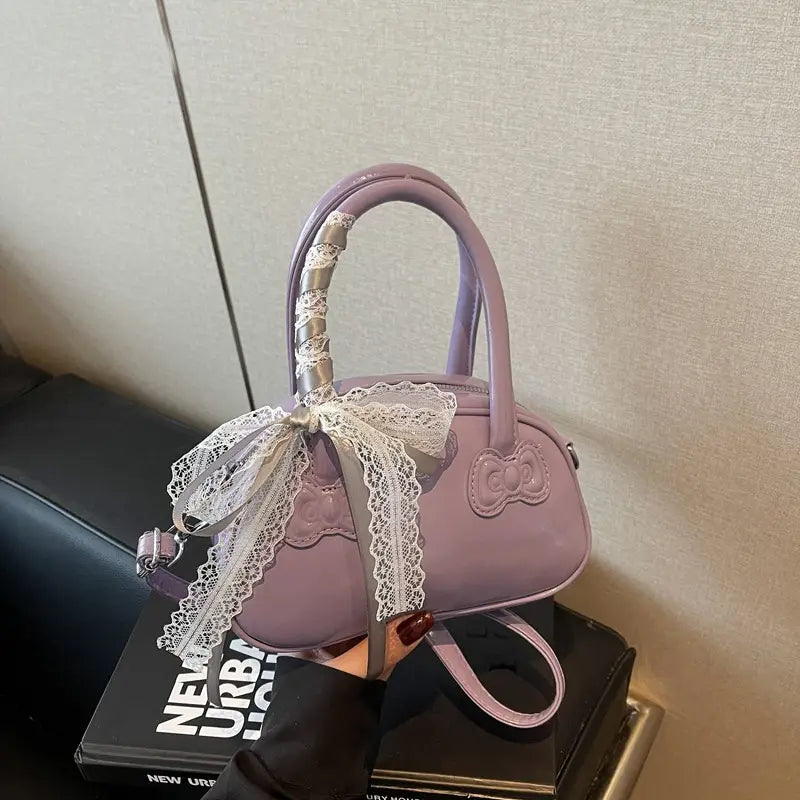 Hello Kitty glossy lace bow crossbody bag in lavender faux leather with a white lace bow on the handle and an embroidered cat face on the front.