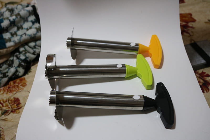 Tres peladores, descorazonadores y herramientas de corte para piña de acero inoxidable con mangos de silicona de colores en verde amarillento y negro.