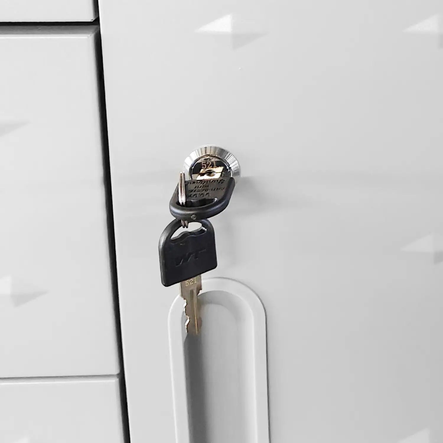 Black key with a silver-toned metal blade inserted into the circular metallic lock of a gray metal tool storage cabinet with wheels and four drawers on a white cabinet door.