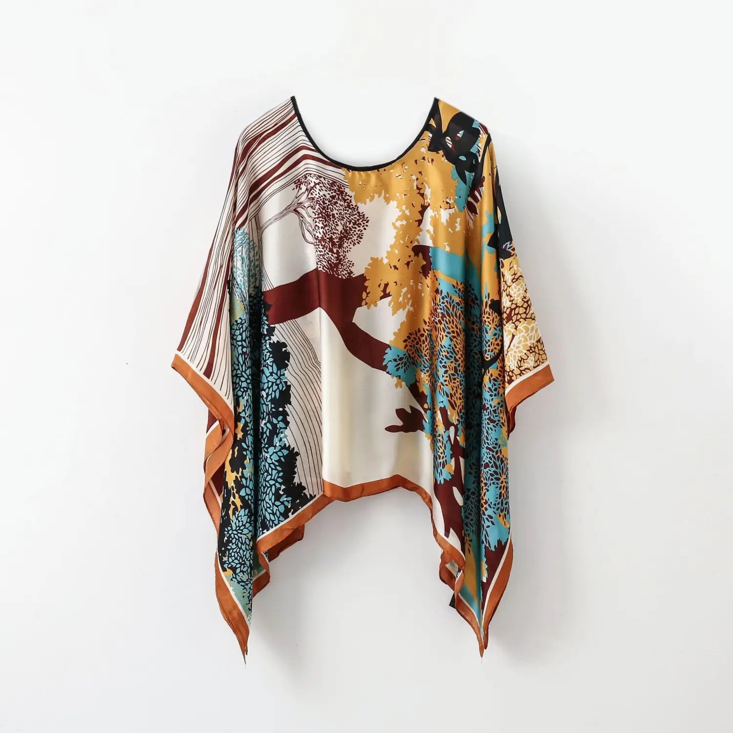 printed silk patterned pullover shawl cape outerwear featuring a flowing oversized silk cape with a vibrant autumnal tree design in shades of gold teal and rust against an off-white background.
