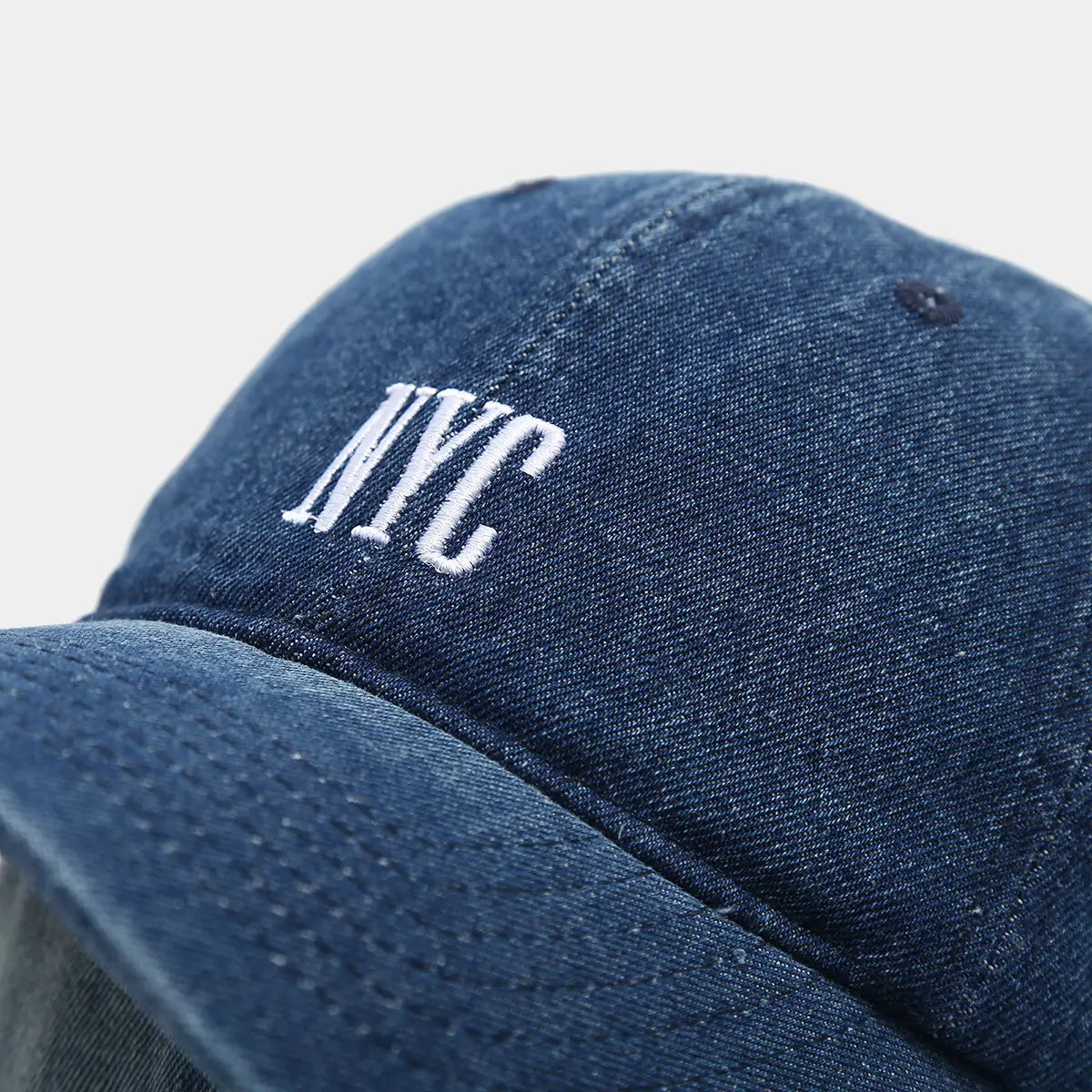 A navy blue denim baseball cap featuring white embroidered nyc lettering in a retro letter embroidery style.