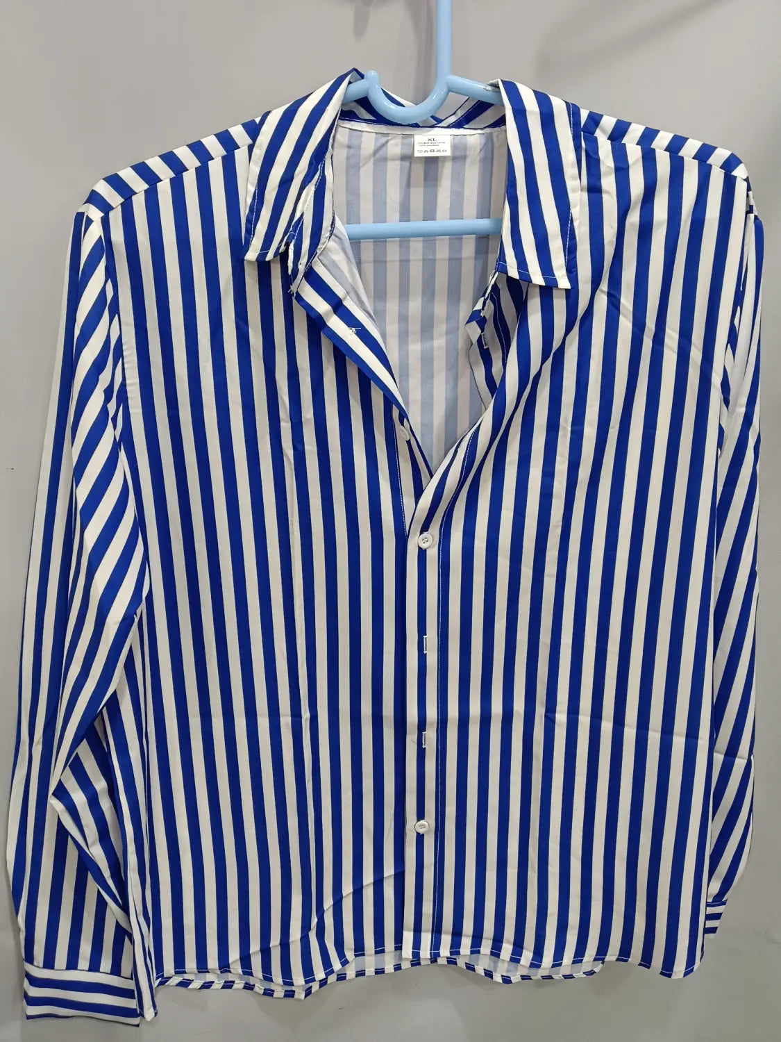 Chemise décontractée à manches longues rayée verticalement bleu et blanc pour hommes, suspendue sur un cintre.