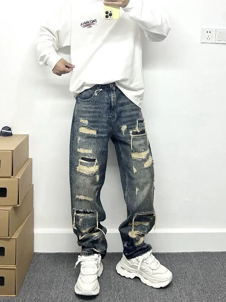 Men’s light blue distressed ripped patch denim jeans featuring dark blue denim with multiple ripped patches and frayed edges.