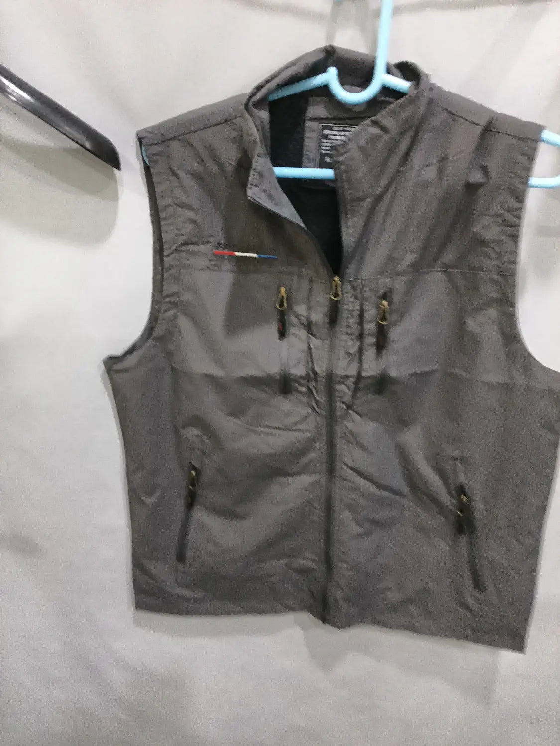 Chaleco utilitario con capucha y múltiples bolsillos para hombre en nailon gris, con cremalleras negras y un bolígrafo guardado en el bolsillo del pecho.