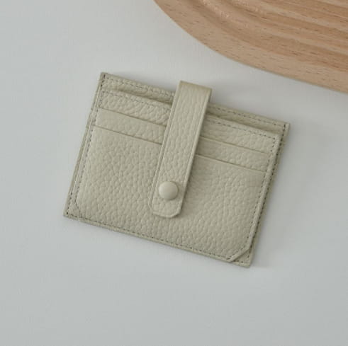 Ultra thin minimalist textured leather card holder in off-white with a matching strap and button closure.
