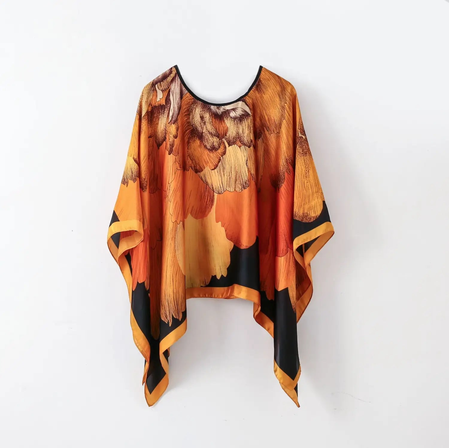 A flowing orange and black floral print silk pullover shawl cape with a rounded neckline for outerwear.