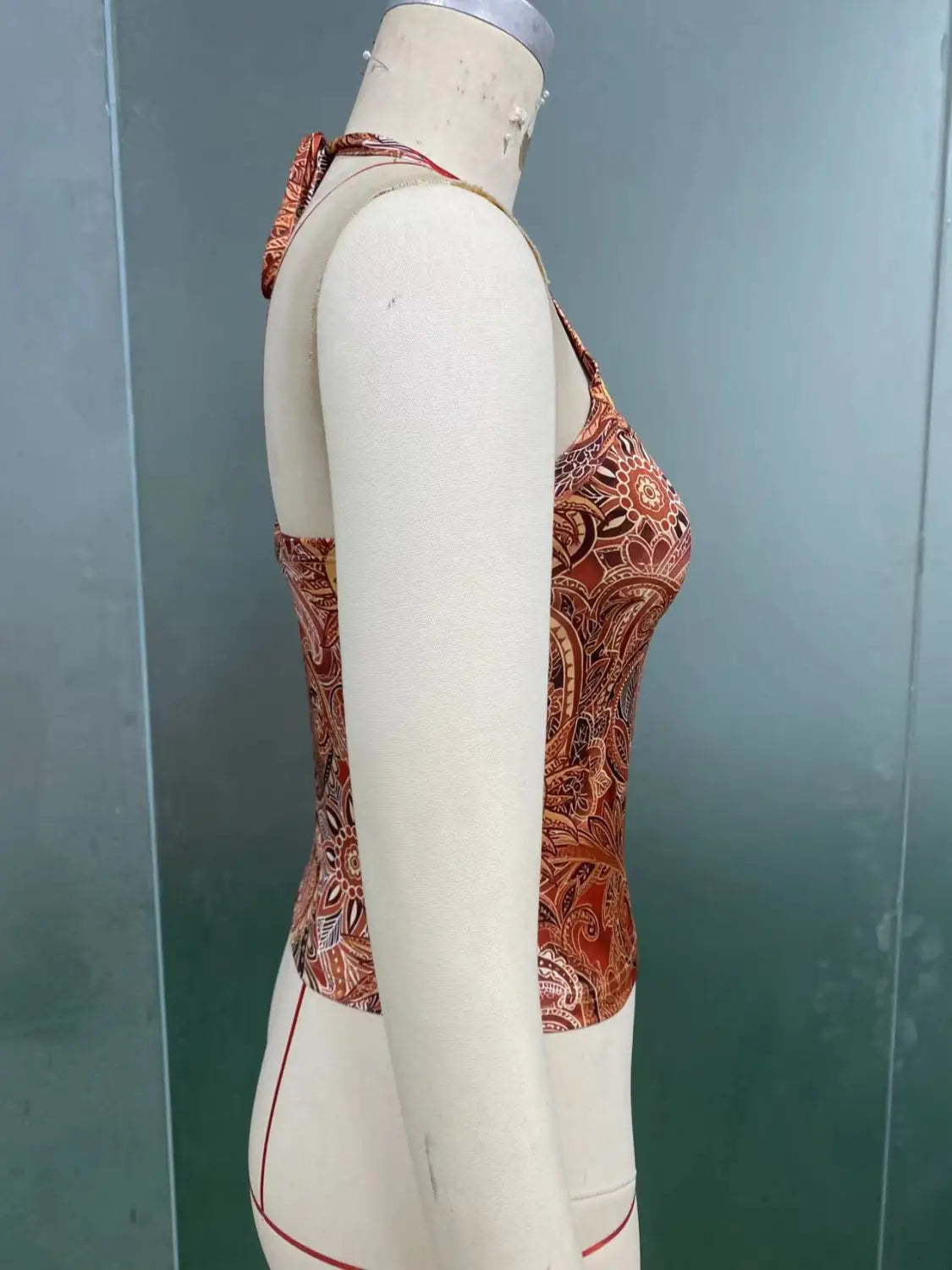Ein tailliert geschnittenes Halterneck-Top mit einem kräftigen Rost- und Braun-Paisley-Muster, auf einer Schneiderpuppe für einen Slim-Fit-Sun-Print-Orange-Look dargestellt.
