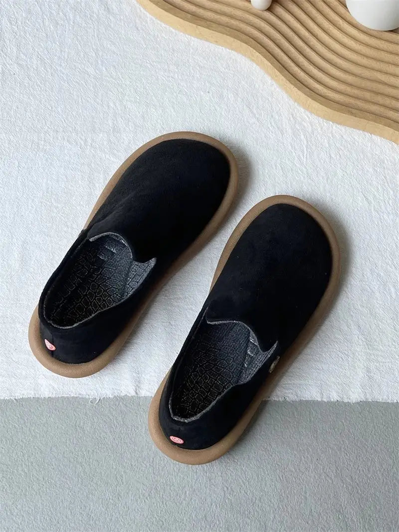 Schwarze Veloursleder-Slipper im Vintage-British-Stil mit niedrigem Absatz mit einer braun wirkenden Gummisohle, von hinten dargestellt.