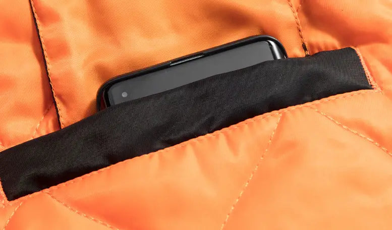 A black smartphone rests in the vibrant orange quilted pocket of the men’s retro loose flight bomber jacket featuring workwear style and textured stitching.