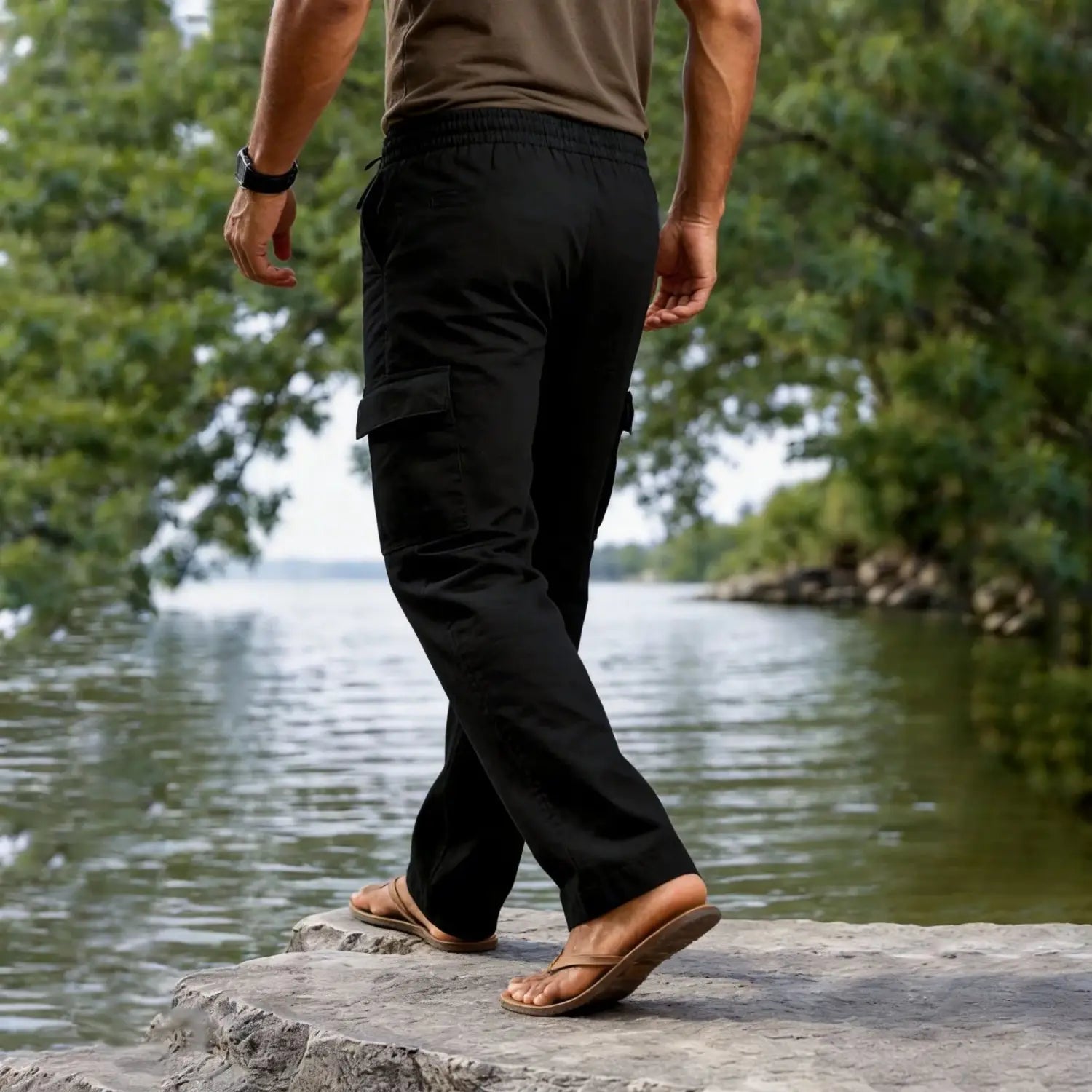Men cotton linen cargo pants casual straight leg drawstring in black with elastic waistband and side pockets worn by a person standing on rocks near water.