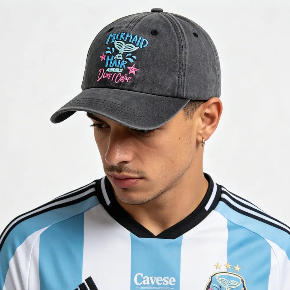 Una gorra tipo béisbol de algodón gris oscuro desgastado con diseño bordado del cabello de sirena en azul, rosa y blanco y texto.