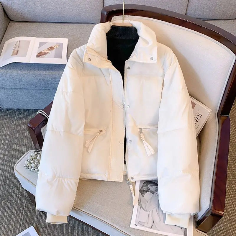 Chaqueta exterior de algodón acolchado para mujer en color crema, con cuello alto, cierre frontal con botones y dos bolsillos laterales con cordones.