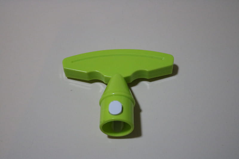 Mango de plástico con forma de T verde lima brillante con un botón circular blanco en el vástago de una herramienta de pelar, descorazonar y cortar piña de acero inoxidable.