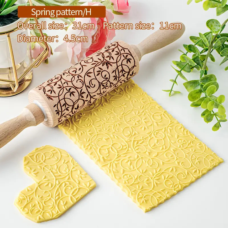 Un rouleau à pâtisserie en bois de hêtre avec des poignées de couleur claire et un motif floral printanier brun foncé gravé, pour imprimer des motifs complexes en relief sur de la pâte jaune.