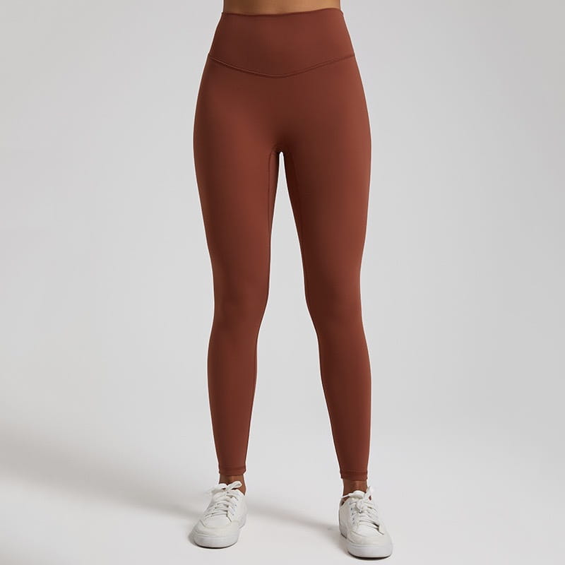 A pair of high waisted stretch fitted leggings in rust color made from stretchy fabric.