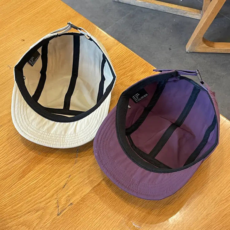 Two quick drying short brim five panel caps in off-white with black trim and purple with black accents suitable for outdoor use.