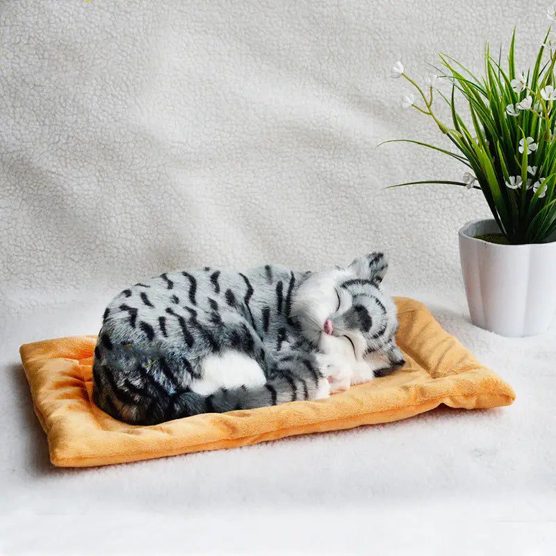 a realistic breathing plush cat figurine in gray and black stripes resting on a soft orange pet bed cushion.