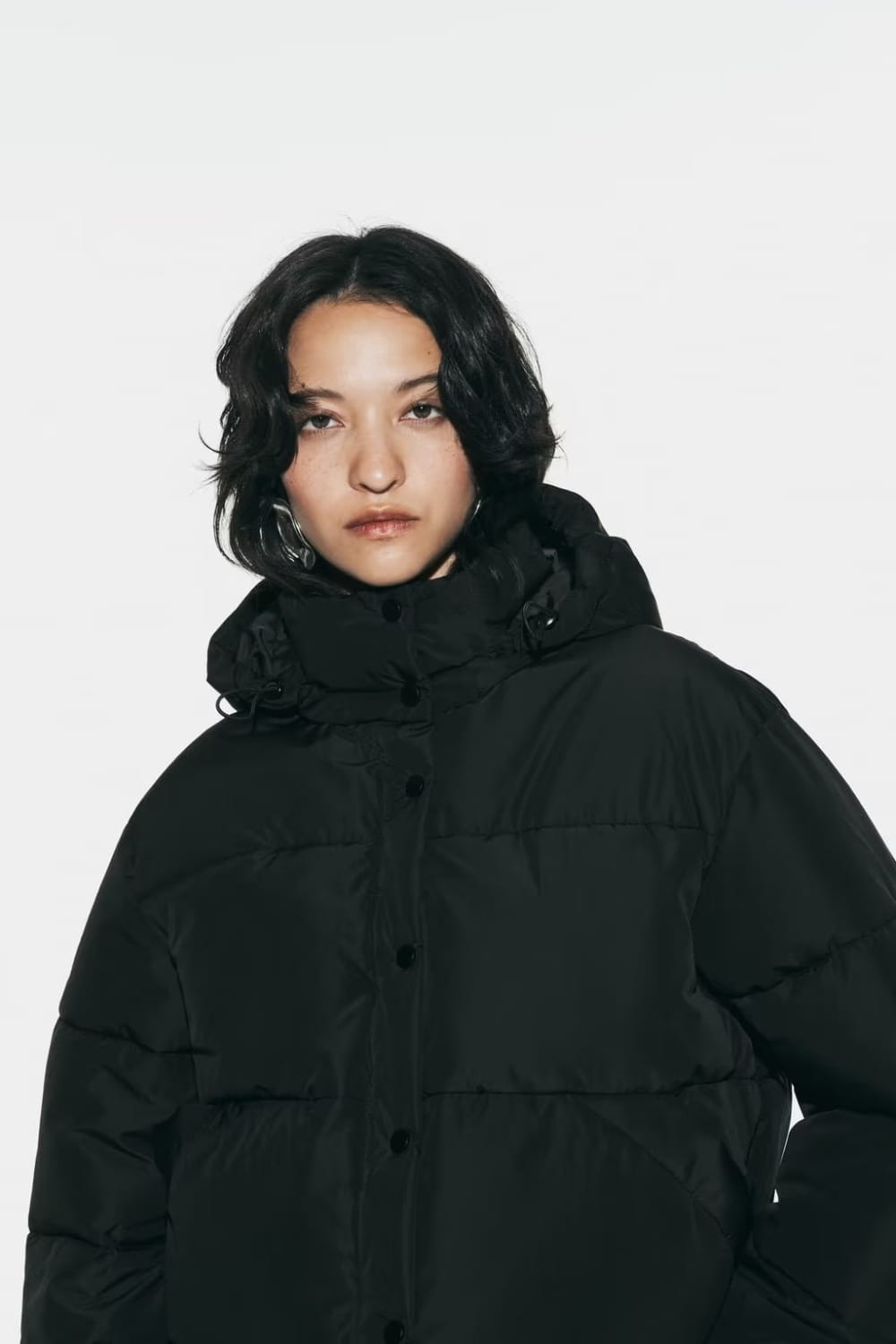 Black quilted hooded puffer coat with button closure and insulated material suitable for cold weather.