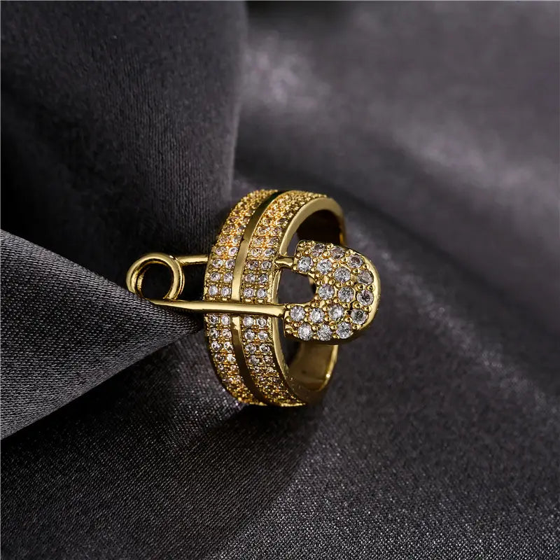 Adjustable gold safety pin ring featuring numerous clear sparkling cubic zirconia stones in a geometric design.