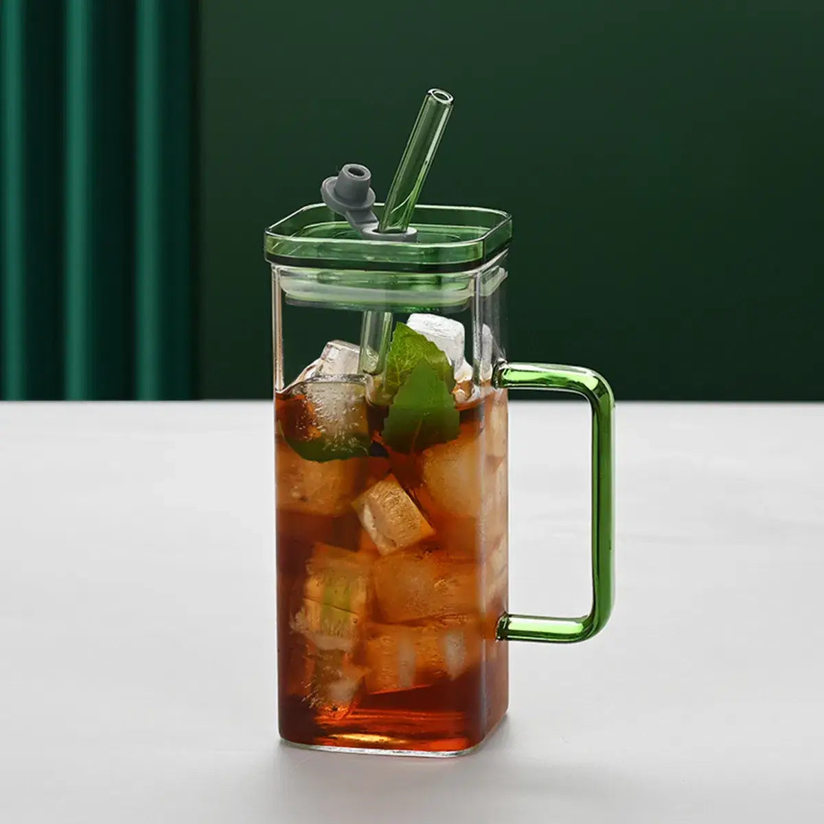 Une tasse carrée en verre transparent de 12 oz avec poignée et couvercle verts, dotée d’une paille intégrée et d’une capacité de 12 oz.