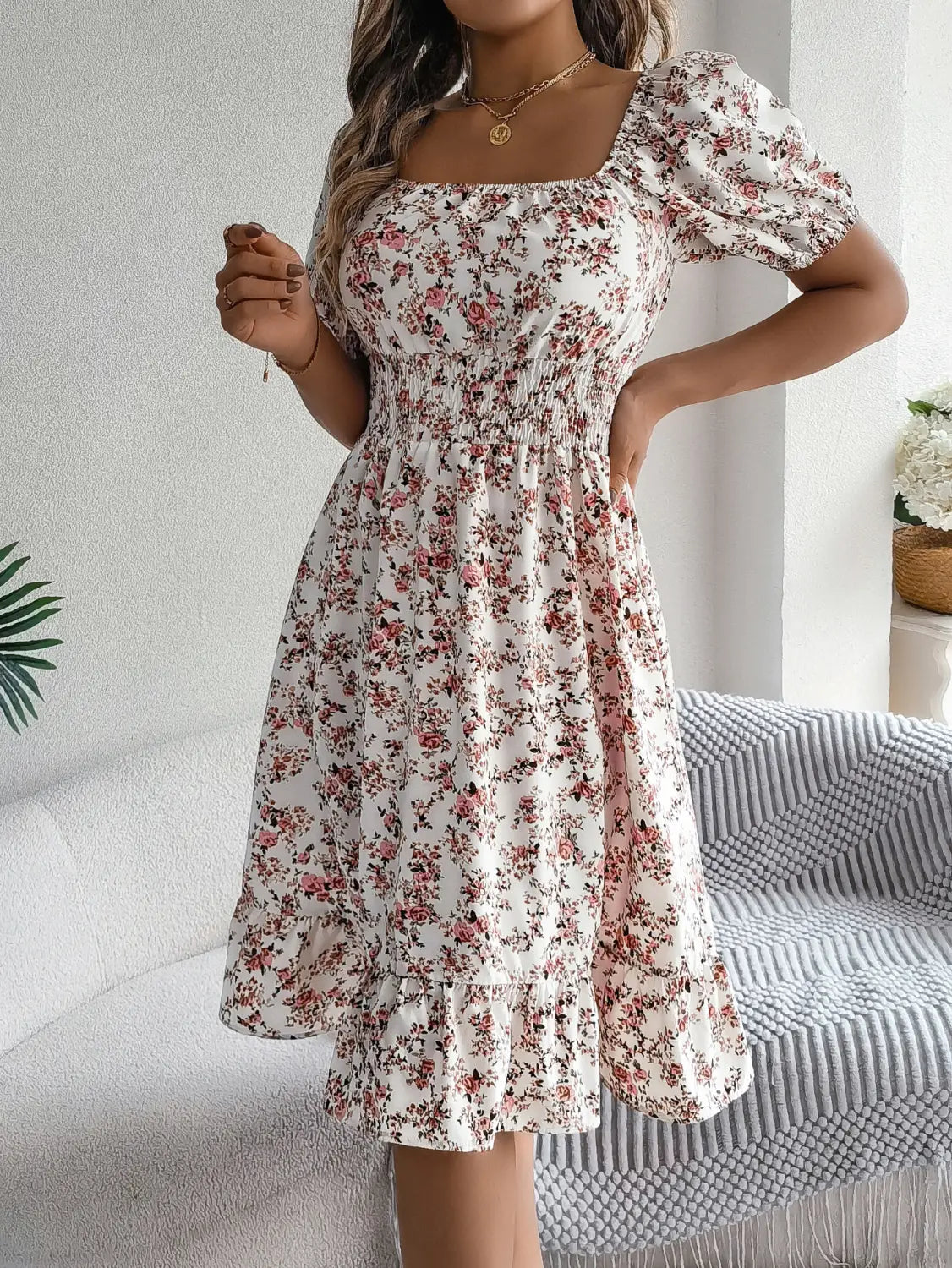 Une femme porte une robe d’été blanche à imprimé floral avec fleurs roses et rouges, encolure carrée, manches courtes bouffantes et ourlet à volants.