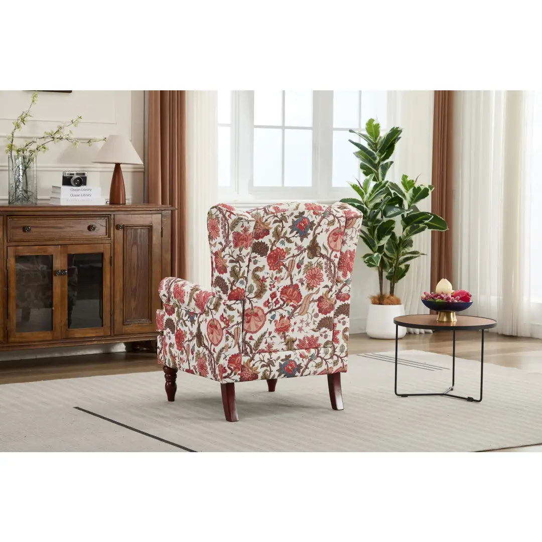 Una silla tipo ala con respaldo capitoné floral, tapizada en un tejido de color crema con diseños botánicos rojos y verdes, con patas de madera oscura retro.