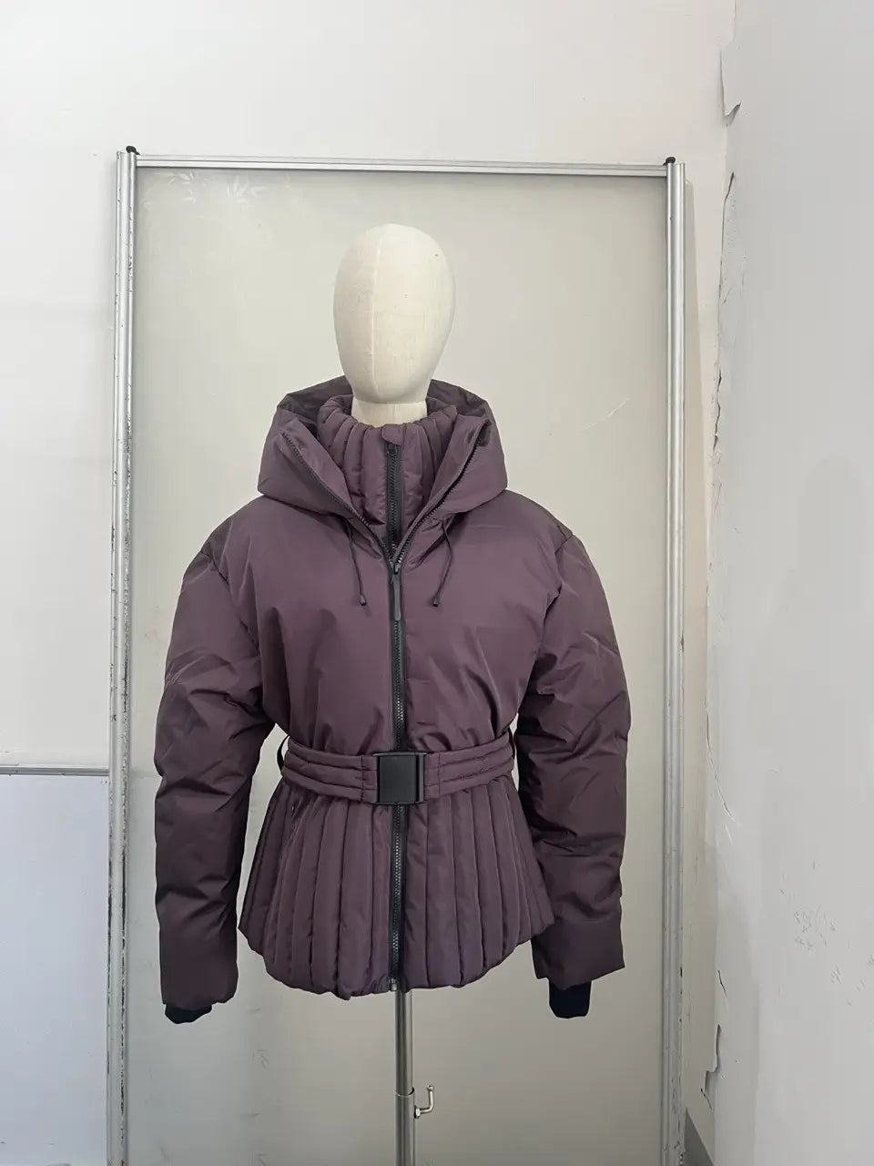 A plush muted purple women’s belted hooded puffer coat featuring a pleated waistband and a hood.
