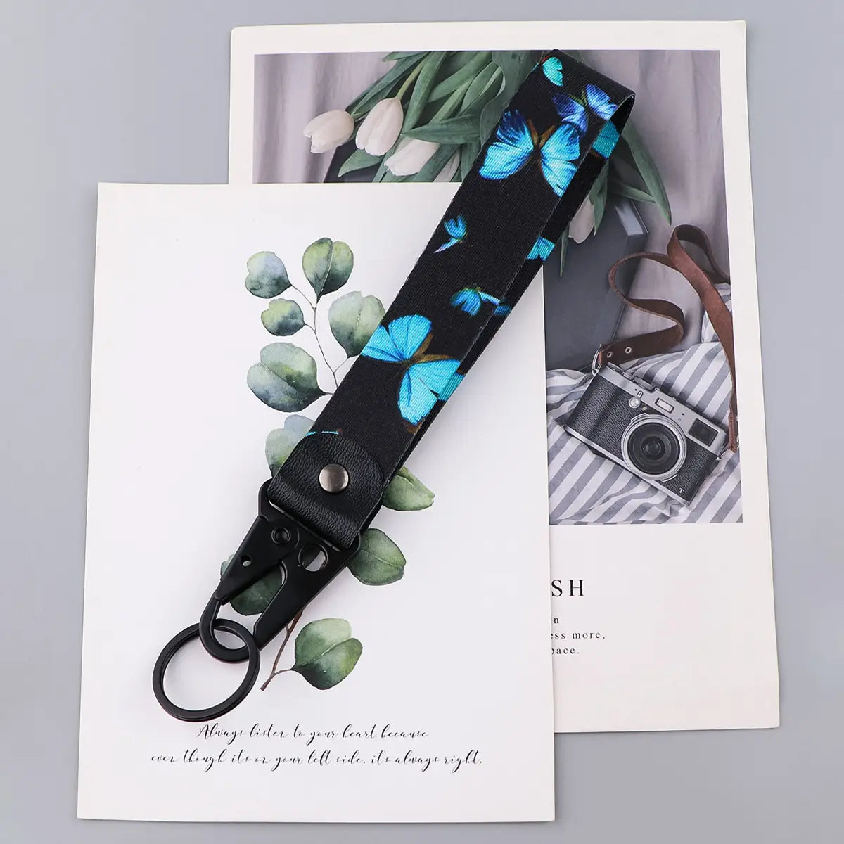 Black wrist strap keychain with vibrant blue butterfly print and black metal clip for secure attachment model Tk57.