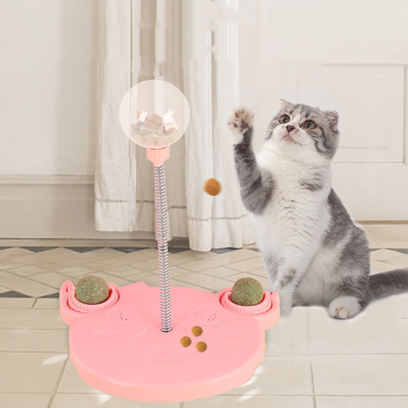Gobelet distributeur de nourriture pour jouet puzzle interactif en plastique rose en forme de chat, avec un mât métallique flexible, une bille transparente sur le dessus, deux billes vertes texturées dans des coupelles latérales, et des friandises dispersées conçues pour stimuler les félins.