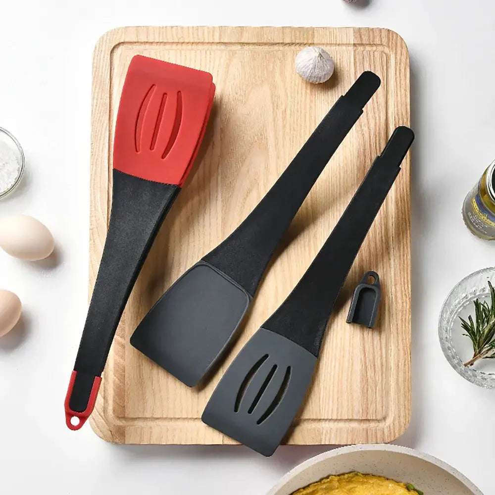 Red and black silicone 3-in-1 slotted spatulas with heat-resistant heads resting on a wooden cutting board