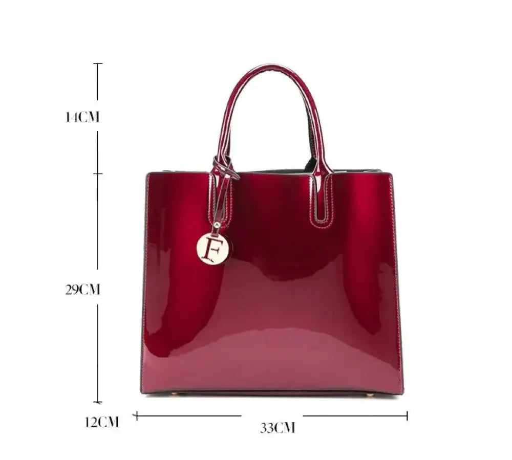 A glossy crimson leather handbag with structured handles and a circular metallic charm from premium 3-piece tote set