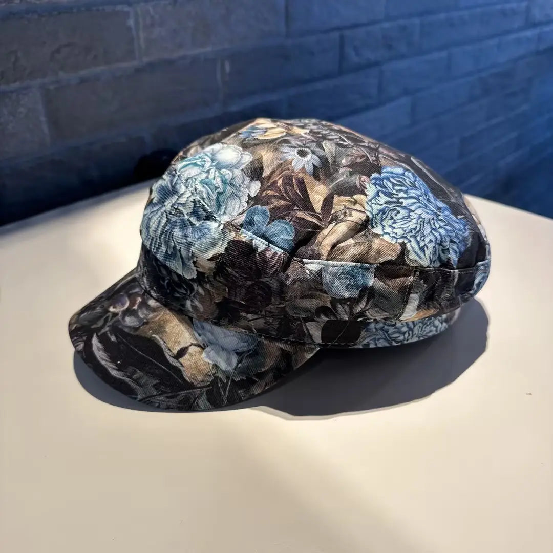Gorra tipo bucket hat floral elegante, estilo coreano, impresa, con grandes flores azules y beige sobre una tela de textura suave, con fondo oscuro.