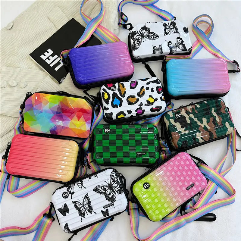 A collection of colorful hard-shell mini suitcases with rainbow straps featuring butterfly, leopard print, camouflage, checkered, and gradient patterns.