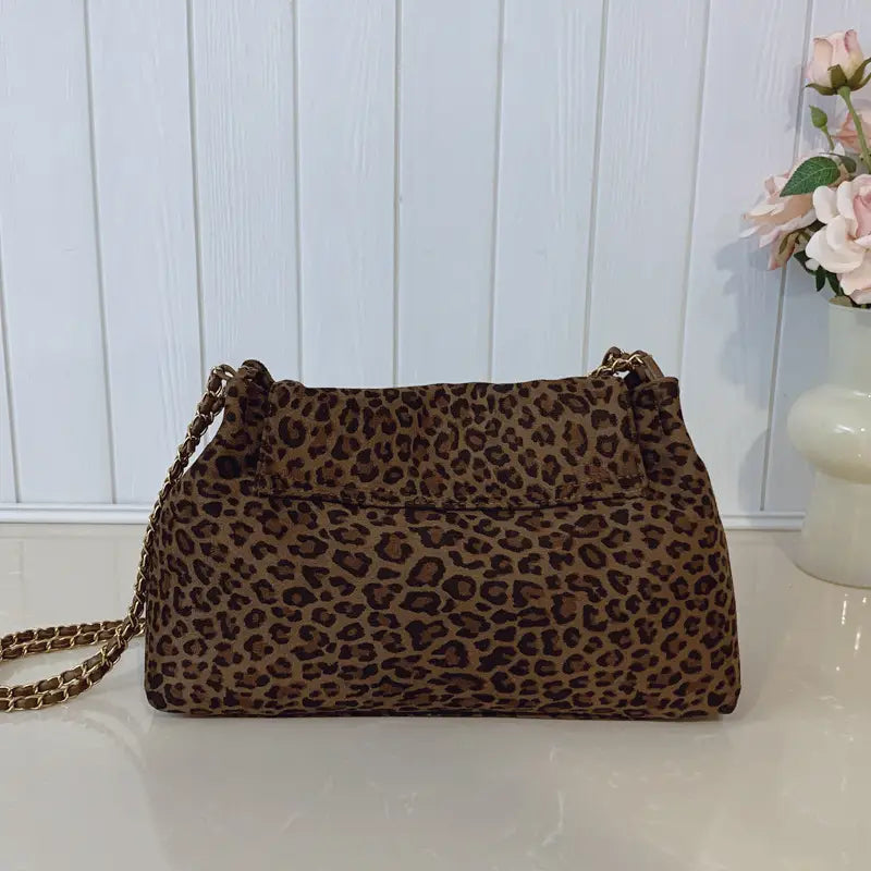 Brown leopard print suede crossbody bag with gold tone chain strap for shoulder wear.