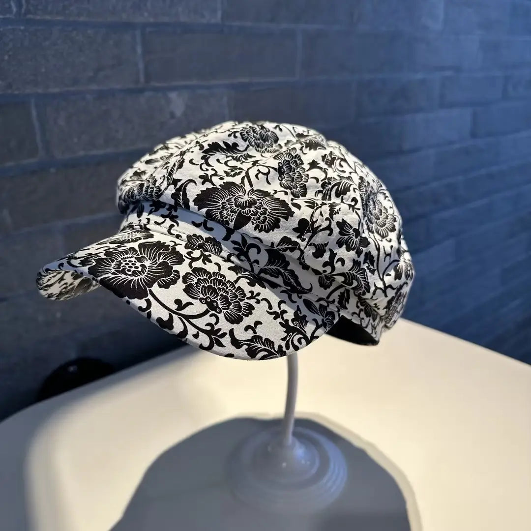 A black and white floral-patterned fabric newsboy cap for women with a structured rounded crown and a short brim.