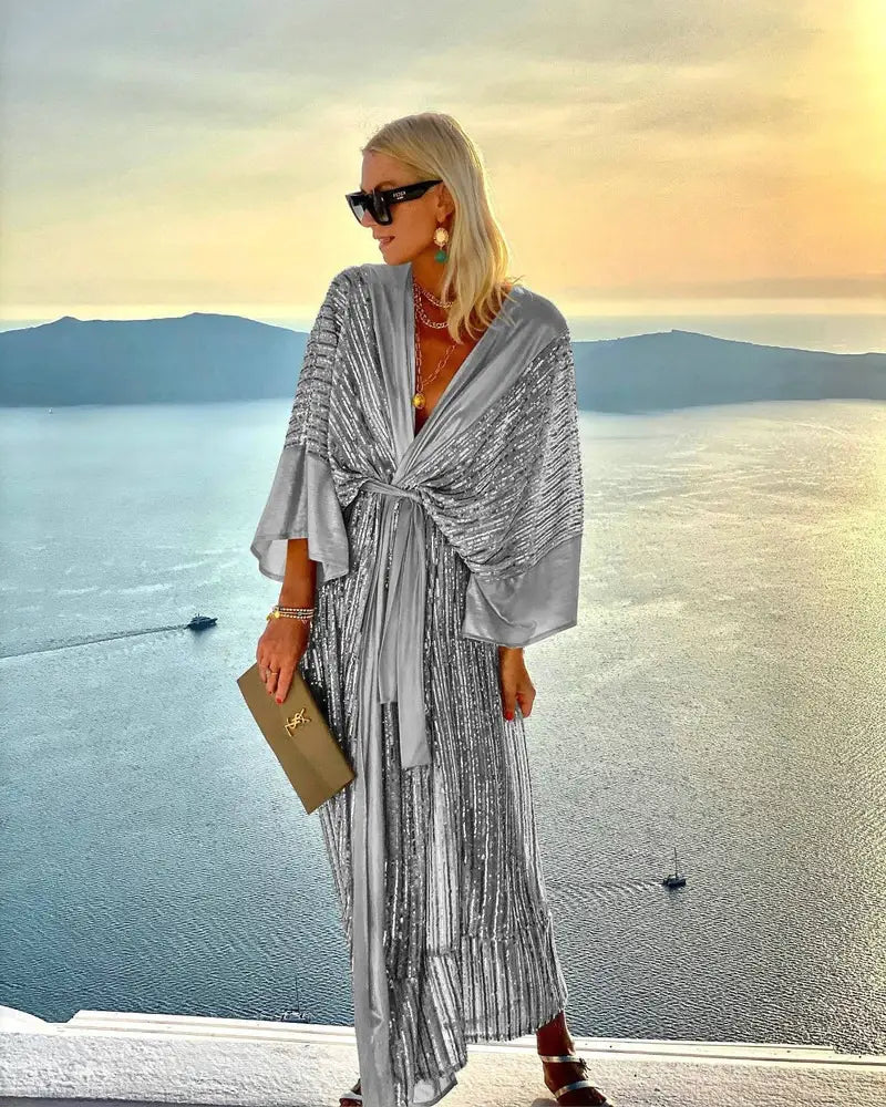 Silver metallic pleated maxi dress with bat sleeves and a draped tie-front design made of sequin fabric.